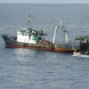 A 50m fishing trawler off the coast of Ghana, patches of rust on its blue hull, a small grey inflatable with US and Ghanaian marines coming up astern. Image by Jeff Atherton/US Navy via Flickr (CC BY-ND 2.0)