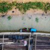 Overhead shot of two men standing in shallow water, bent over repairing a large wooden canoe. Image by Bolaji Eiseke via Wikicommons (CC BY-SA 4.0)