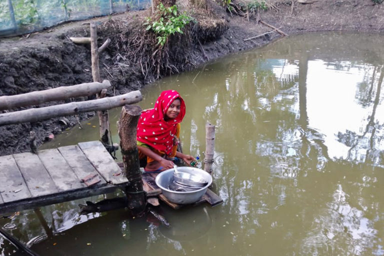 A woman in Satkhira washes dishes in a pond.